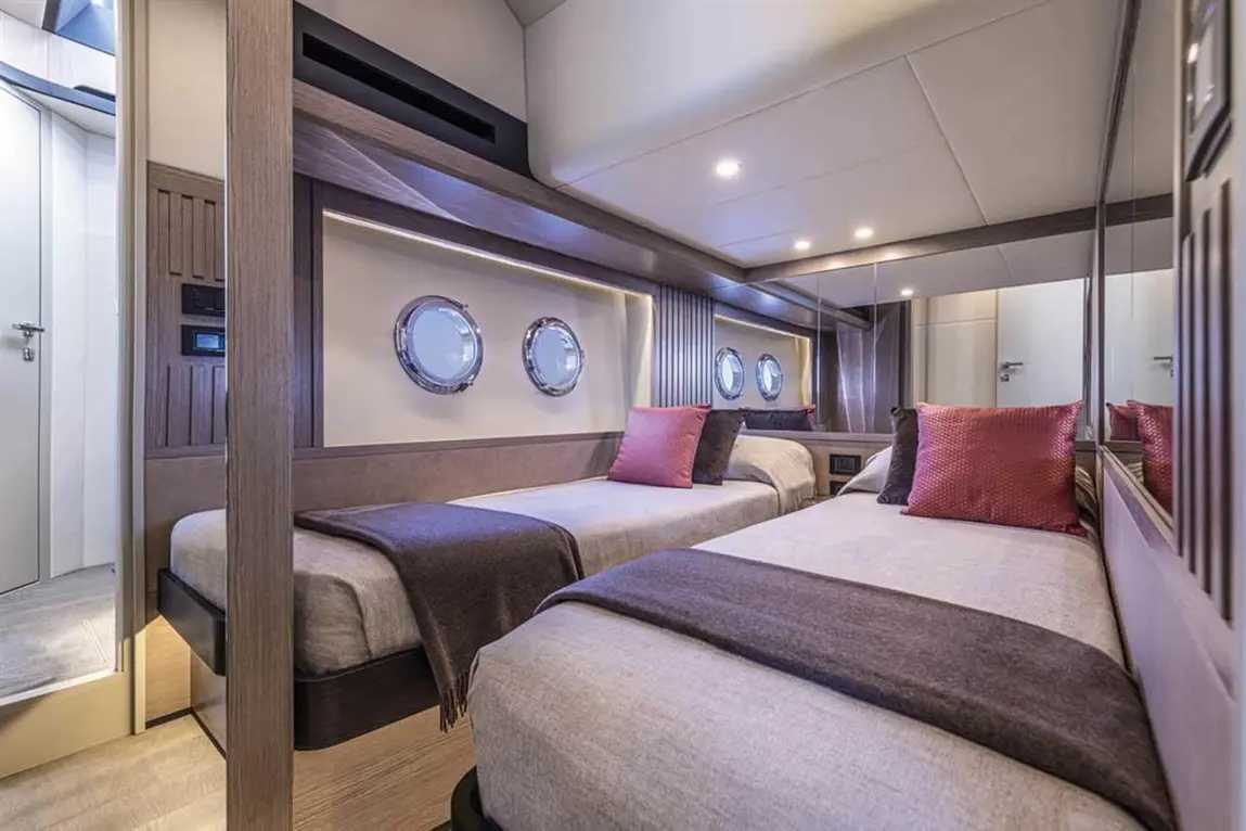 Modern twin bedroom with two beds, stylish decor, and round porthole windows, highlighting luxury yacht accommodation.